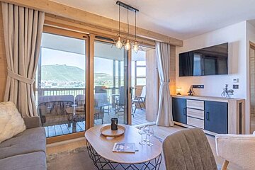 Cozy living room with wood accents, a stylish coffee table, and large glass doors opening onto a scenic mountain-view balcony.
