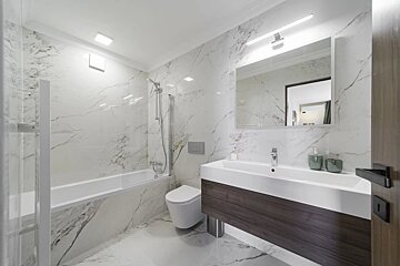 Sleek modern bathroom with white marble tiles, a bathtub, a toilet, and a floating dark wood vanity with a large mirror.
