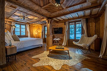 A cozy, all-wood chalet bedroom with a bed, windows showing snow, and rustic furniture, creating a warm winter retreat.