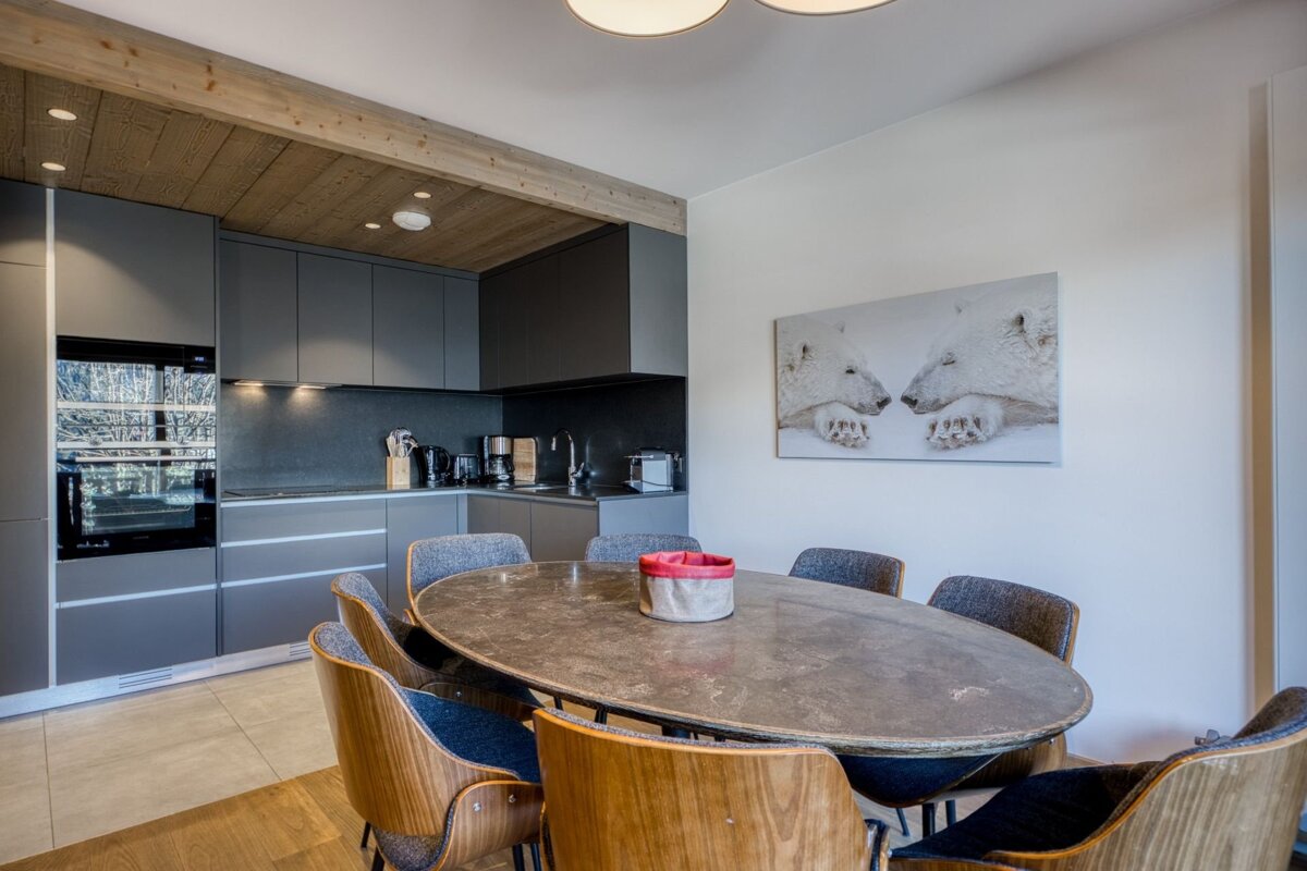 A modern dining area with an oval table, wooden chairs, grey kitchen cabinets, and polar bear wall art.