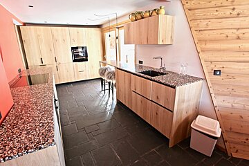 Modern kitchen featuring light wood cabinets, granite countertops, dark slate tile flooring, and a slanted wooden wall.