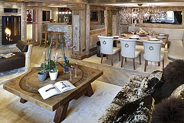 A luxurious rustic chalet features a cozy fireplace, bar, and elegant dining area. Rich wood, stone, and chic furnishings create a warm ambiance.