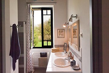 A bathroom with two sinks and two mirrors has a picture on the wall that says margot