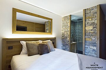 Cozy alpine bedroom featuring a backlit wooden headboard, large mirror, and an adjacent stone-walled bathroom.