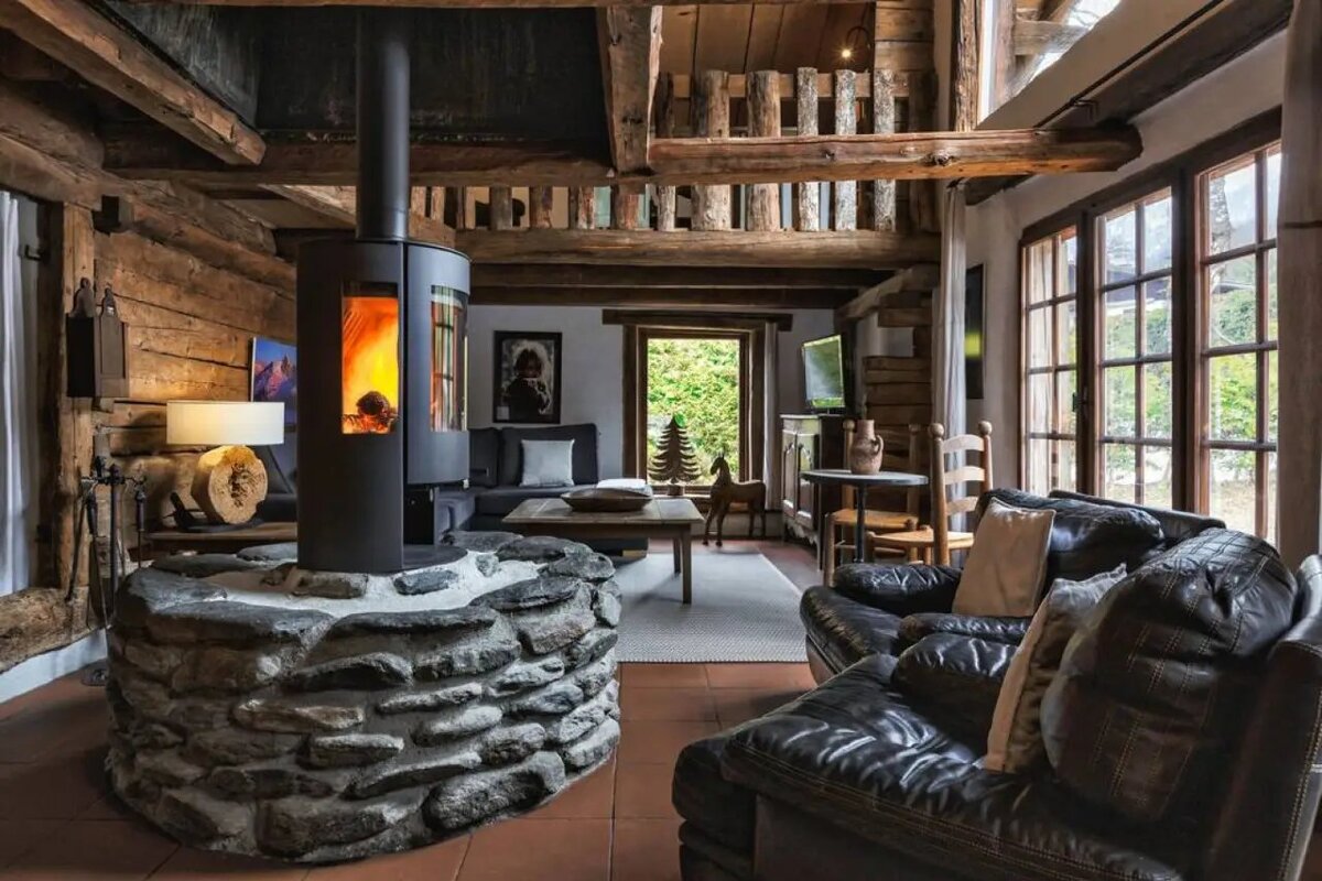 Cozy rustic cabin interior with a central stone fireplace, leather sofas, and exposed wooden beams.