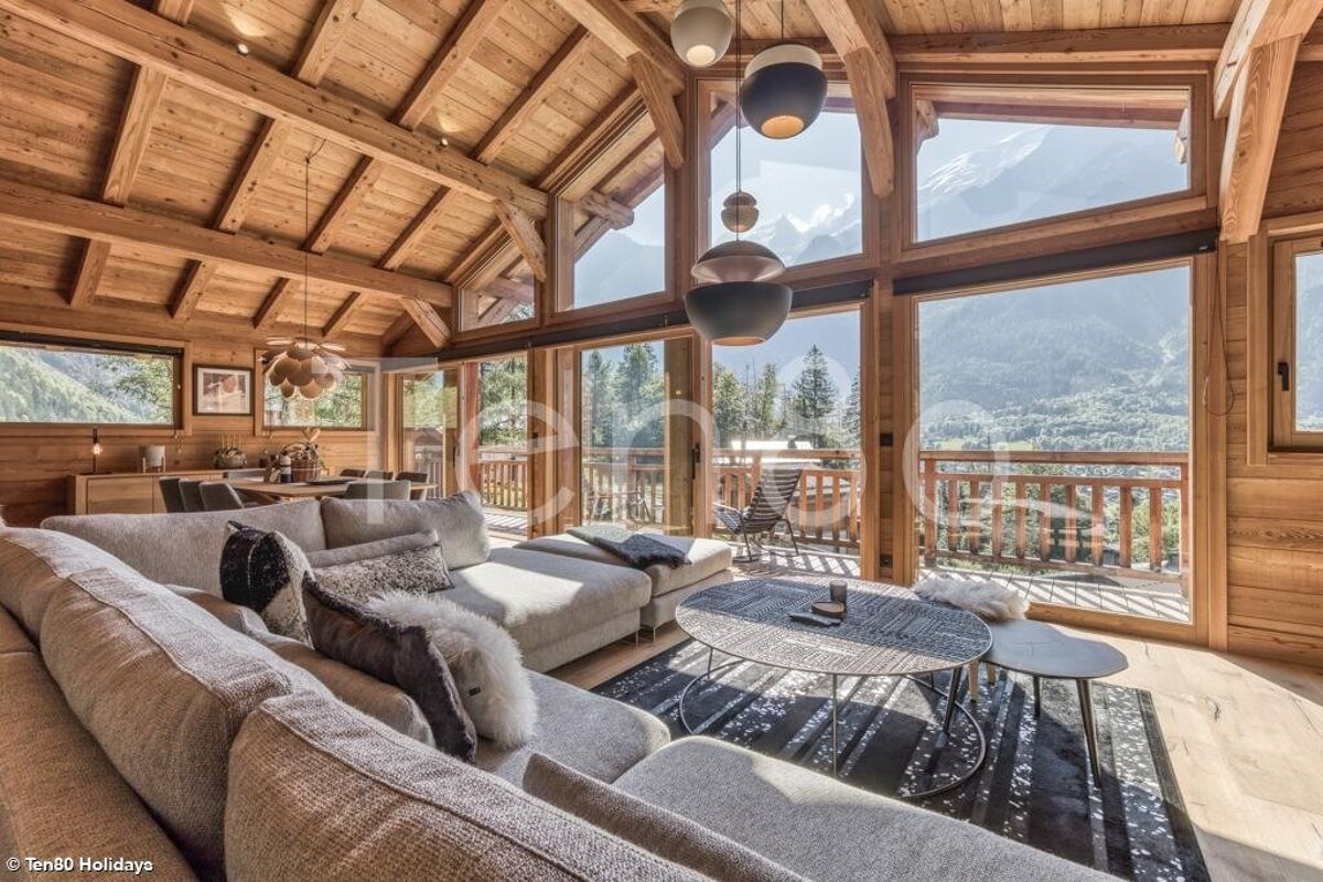 Cozy wooden chalet living room with a large sofa and huge windows overlooking stunning mountain views.