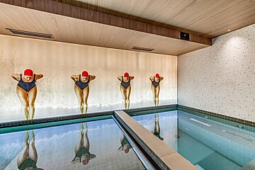 An indoor swimming pool with a mural of four female swimmers in red caps, their figures reflected in the calm, clear water.