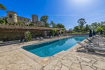 A sunny swimming pool and stone patio lined with lounge chairs, overlooked by a historic stone castle.