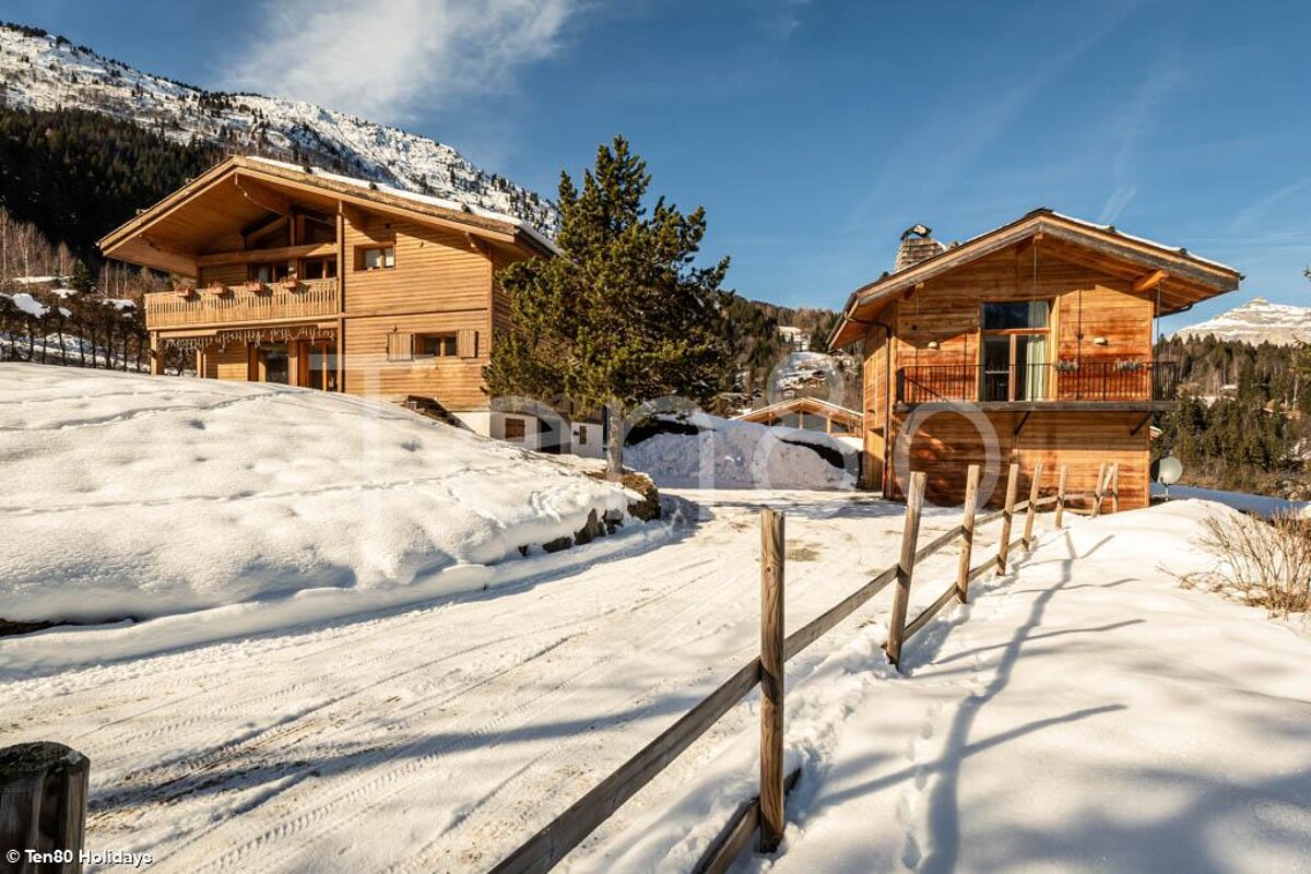 A snowy landscape with two wooden houses and a fence