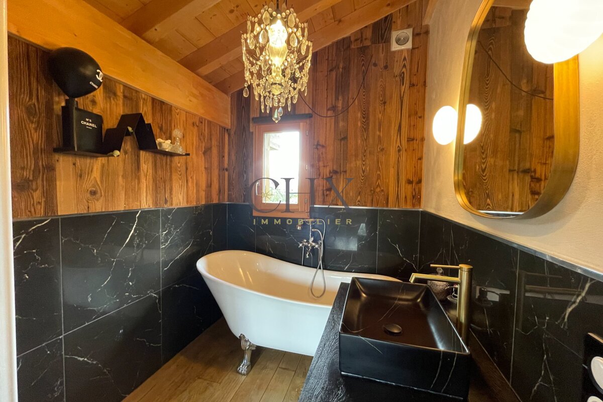 Rustic luxury bathroom featuring a white clawfoot tub, black marble tiles, wooden walls, and a crystal chandelier.