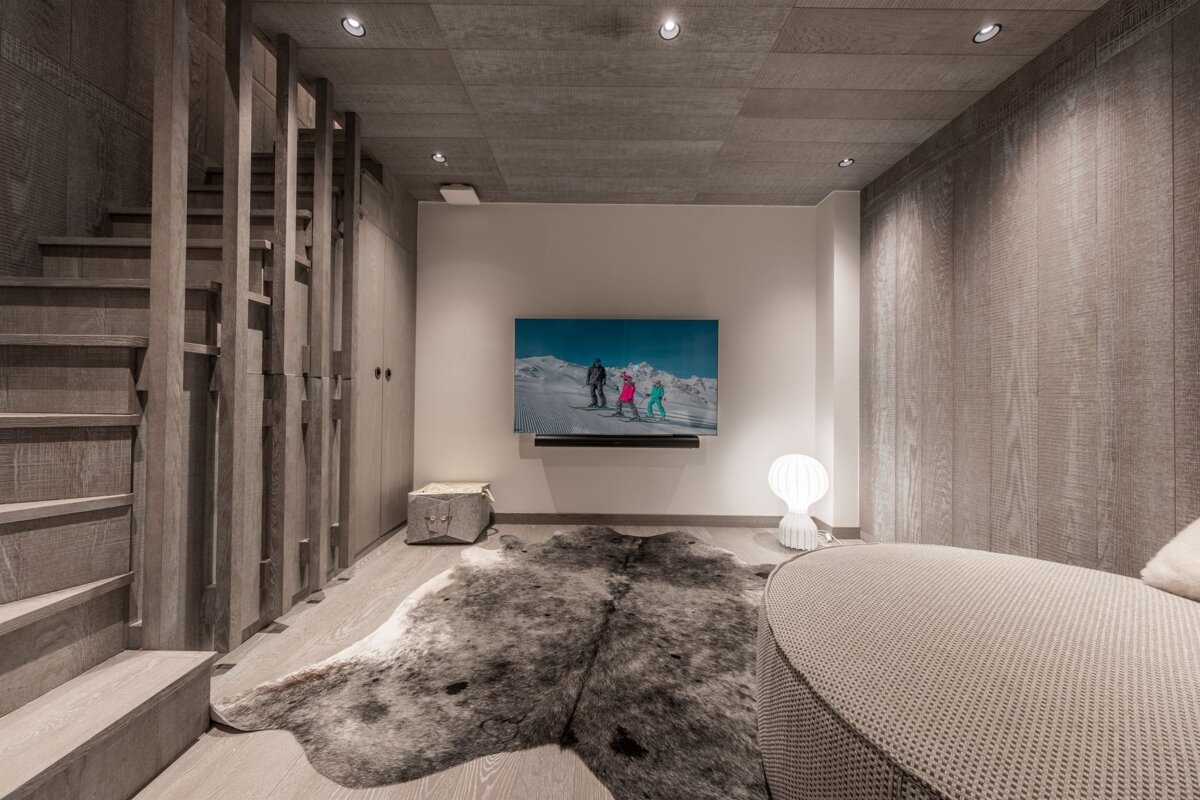 Stylish modern room with light wood accents, TV showing skiers, a cowhide rug, and a sleek wooden staircase.