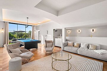 Bright, modern living room with a pool table, large window showing an outdoor view, and a comfy seating area on a patterned rug.