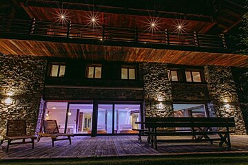 A house with a wooden roof and a stone wall is lit up at night