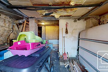 A cluttered, unfinished basement or storage room with large tanks, stacked colorful sleds, tools, and exposed pipes/insulation on the ceiling.