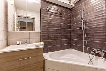 A modern bathroom featuring a wooden vanity with a white sink, mirrored cabinet, and a bathtub with a shower, all surrounded by contemporary tiles.