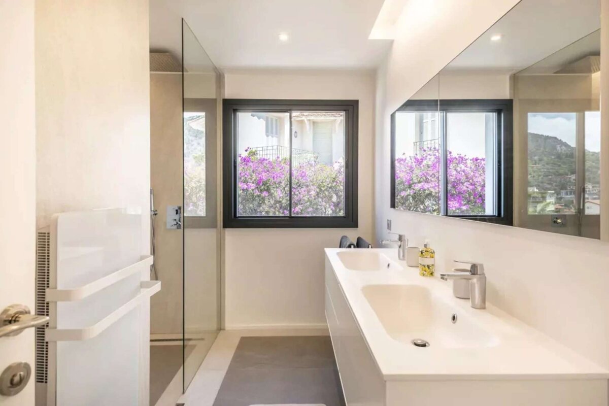 A bathroom with two sinks and a window with purple flowers