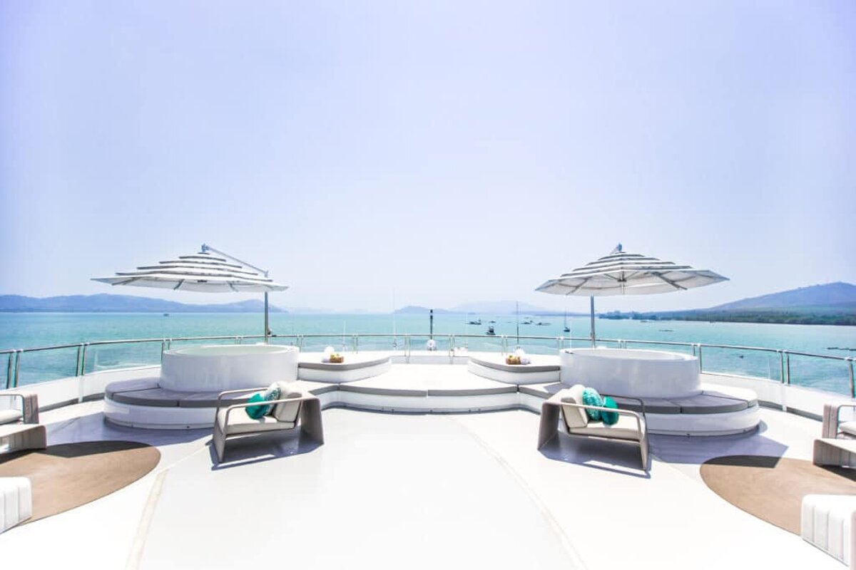 A boat deck with a hot tub and umbrellas overlooking the ocean