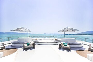 A boat deck with a hot tub and umbrellas overlooking the ocean