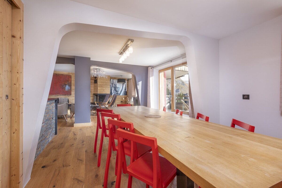 Modern dining room featuring a long wooden table with bright red chairs, hardwood floors, and a stylish curved archway.