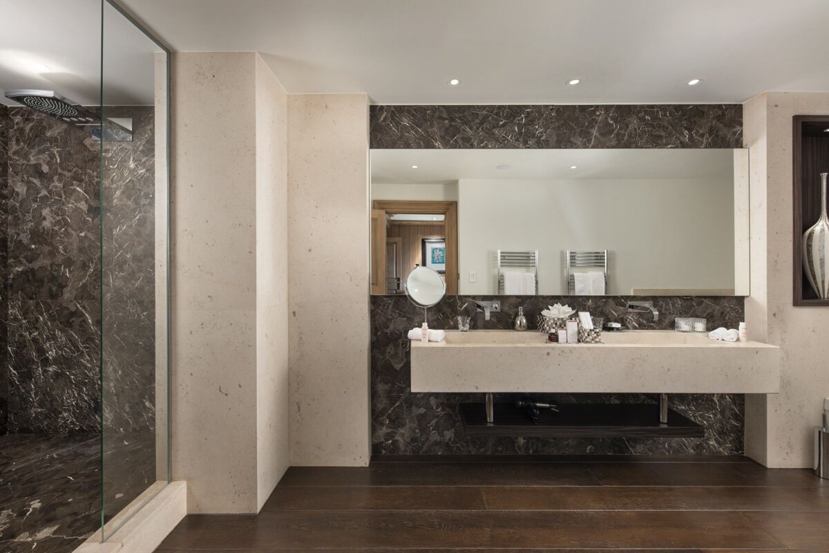 Luxurious modern bathroom with a dark marble shower & backsplash, light floating double vanity, large mirror, and dark wood floors.