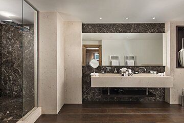 Luxurious modern bathroom with a dark marble shower & backsplash, light floating double vanity, large mirror, and dark wood floors.