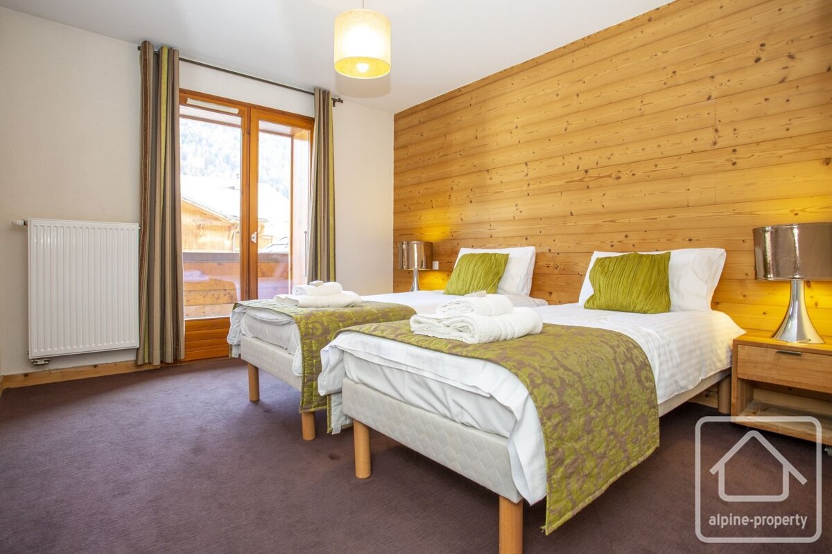 Cozy wood-paneled bedroom with twin beds featuring green accents, a balcony door, and a purple carpet.