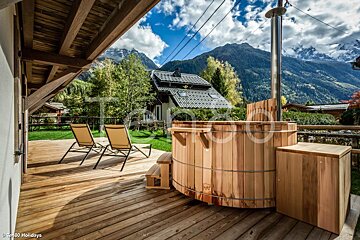 A wooden hot tub on a deck with mountains in the background