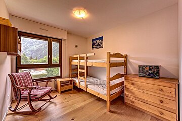 Cozy cabin bedroom featuring wooden bunk beds, a striped rocking chair, a dresser, and a large window with scenic mountain views.