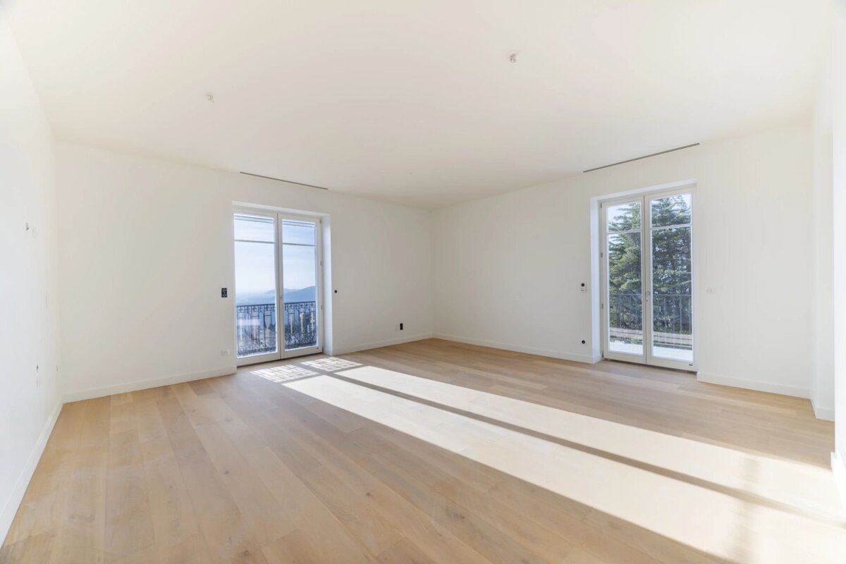 An empty room with white walls, light wood floors, and sunlight streaming through two sets of French doors.