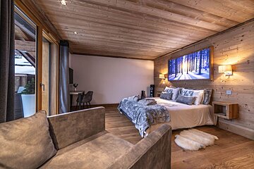 A luxurious, cozy wood-paneled bedroom featuring a large bed, snowy forest wall art, balcony access, and a seating area.