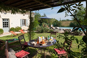 A patio area with a table and chairs and a pool in the background