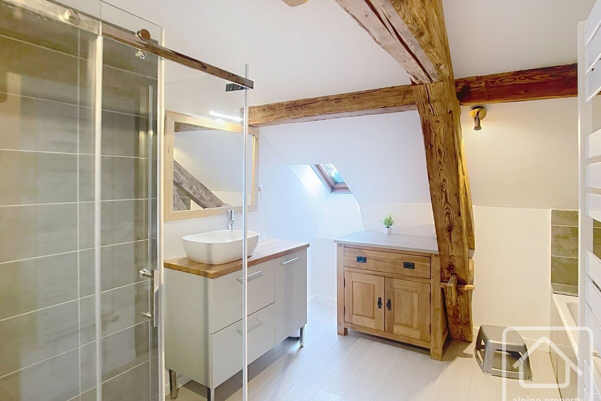 Bright, modern bathroom featuring a glass shower, vanity, exposed wood beams, and a skylight in the sloping ceiling.