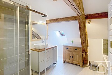 Bright, modern bathroom featuring a glass shower, vanity, exposed wood beams, and a skylight in the sloping ceiling.