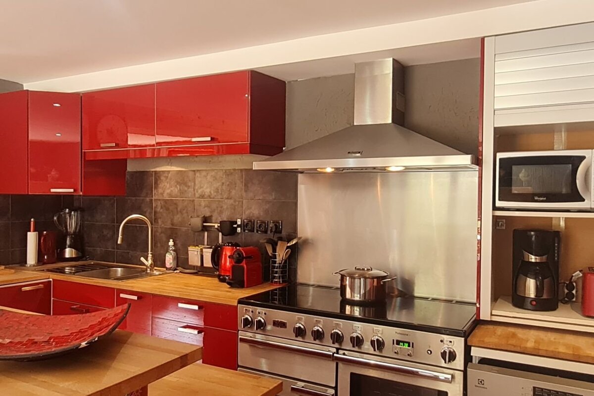 Modern kitchen with vibrant red cabinets, stainless steel appliances, a large stove, and wooden countertops.