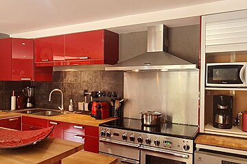 Modern kitchen with vibrant red cabinets, stainless steel appliances, a large stove, and wooden countertops.