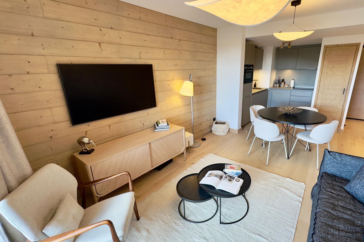 A stylish, open-concept living space featuring wood-paneled walls, a modern kitchen, dining area, and a comfortable living room with light wood floors.