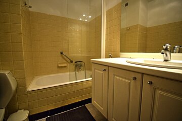 Yellow-tiled bathroom featuring a bathtub with a glass screen, a white vanity with a sink, and a large mirror.