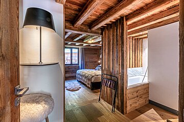 A cozy, rustic bedroom with extensive wood paneling, exposed beams, a bed, and a partial view into a modern bathroom with a tub.