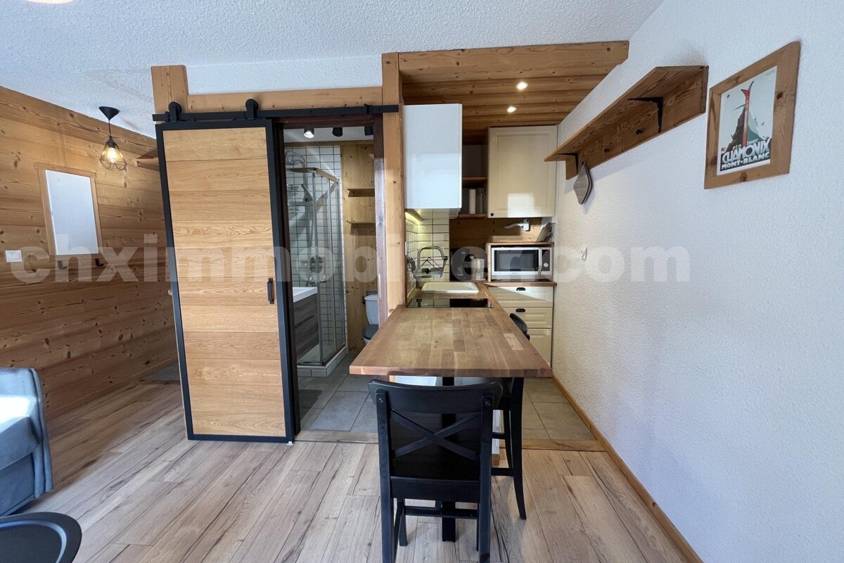 A modern rustic studio with a kitchenette and dining bar, wood-paneled walls, and a bathroom behind a sliding barn door.