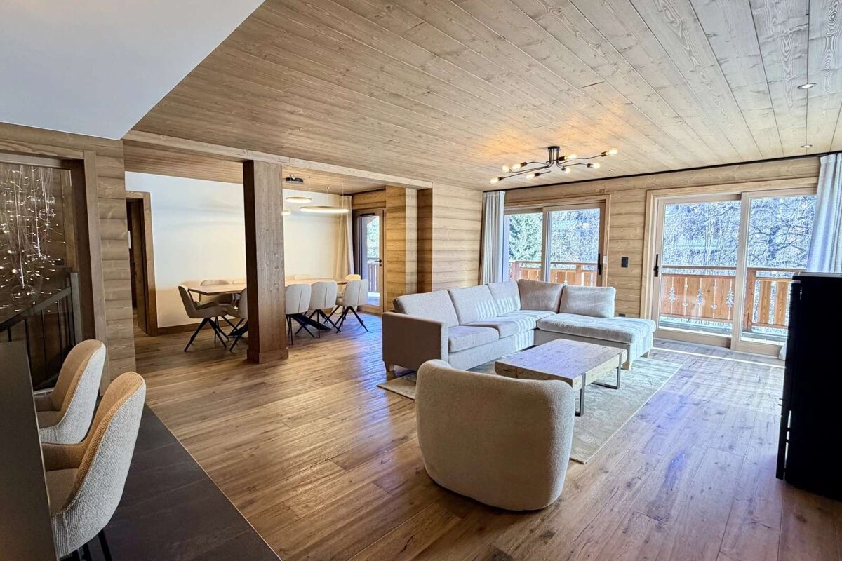 A warm, open-plan living and dining room featuring extensive wood paneling, modern furniture, and large windows overlooking a snowy landscape.