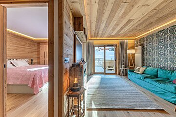Cozy wooden cabin interior showing a bedroom with a pink bed and a living area with a teal sofa and patterned wallpaper.