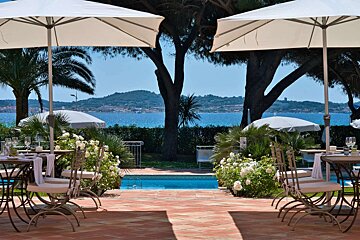 A patio with tables and chairs and umbrellas overlooking a pool