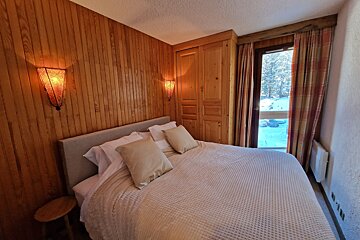 Warm, wood-paneled bedroom with a comfy bed, built-in closet, and a window revealing a snowy outdoor scene.