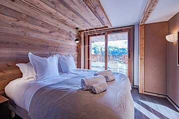 Cozy chalet bedroom with wood paneling, a large bed, and sliding glass doors opening to a snowy mountain view.