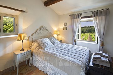 A bedroom with a large bed and a window with a vineyard in the background