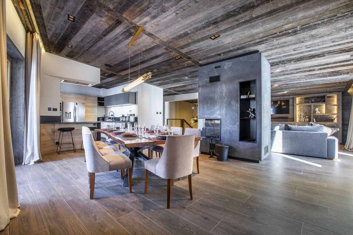 Modern chalet dining room with a rustic wood ceiling, slate fireplace, and stylish dining table.