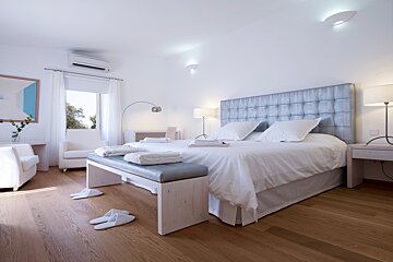 A bedroom with a large bed and a bench with slippers on it