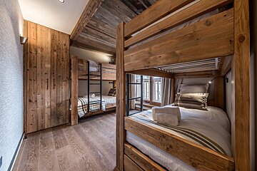 Cozy chalet bunk bedroom with multiple wooden bunk beds, wood-paneled walls/ceiling, and striped/plaid bedding, offering a rustic feel.