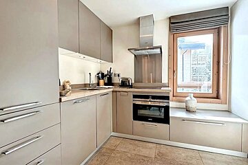 A modern L-shaped kitchen featuring sleek beige cabinets, stainless steel appliances, a large window, and tiled flooring.
