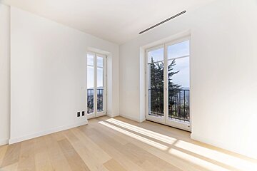 Bright, empty room with light wood floors, white walls, and two French doors opening to scenic balcony views.